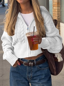 Dettaglio di un cardigan bianco a trecce con cerniera e cappuccio in un contesto urbano