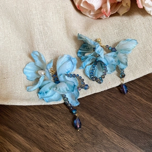 Blue fabric flower earrings with crystal drops and pearls on a rustic wood surface