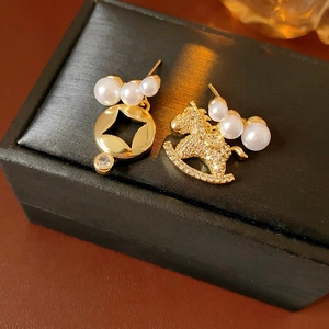 Détail de boucles d'oreilles cheval asymétriques avec finition dorée, perles et zircones