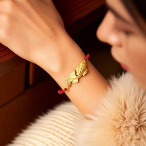 Detailed macro view of a gold koi carp pendant on a red braided bracelet for women
