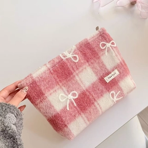 Close-up of pink checkered plush makeup bag with white embroidered bow detail