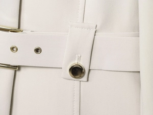 Détail du tissu du blazer crème avec une boucle de ceinture et des boutons dorés polis