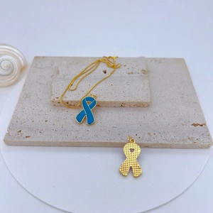 Detailed view of blue enamel ribbon pendant and gold hollow ribbon charm on stone base