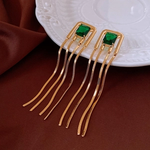 Macro shot of gold tassel earrings with green emerald-cut stones on white porcelain