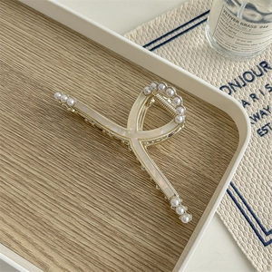 Detail of gold metal hair claw clip with pearl trim on a wooden tray with elegant decor
