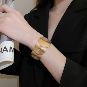 Detail of gold geometric textured open cuff bracelet paired with a black blazer suit