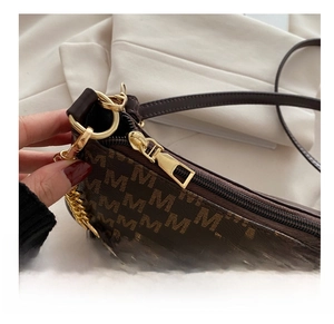 Close-up of smooth gold zipper and luxury M-letter print on dark brown underarm bag