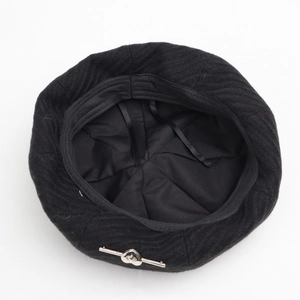 Detail of black beret featuring silver heart buckle and textured herringbone fabric