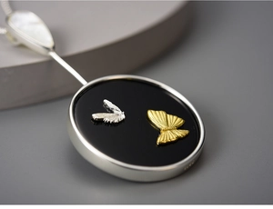 Macro shot of S925 silver butterfly pendant with gold and silver wings on black base