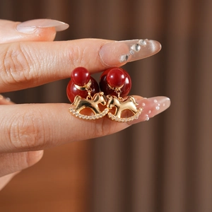 Macro detail of red double-bead earrings featuring a gold rocking horse pendant with crystals