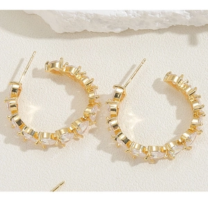 Close-up of gold C-shaped earrings with pear-cut zircon stones on a white stone base