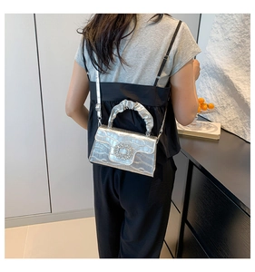 Sac argenté motif crocodile avec boucle en strass et anse plissée porté par un modèle