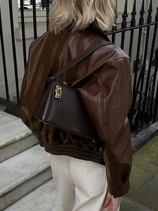 Street style shot of a luxury dark brown leather handbag with gold metal clasp and logo