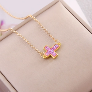 Minimalist gold necklace with a sparkling pink glitter cross pendant on a beige background