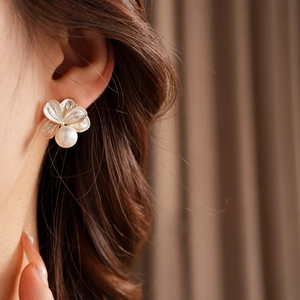 Gros plan d'une boucle d'oreille fleur en perle plaquée or portée par un modèle