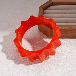 Detailed close-up of orange-red acrylic bangle with marble texture on wood tray
