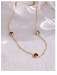 Detail of a thin gold titanium necklace featuring three colorful bezel-set round gemstones