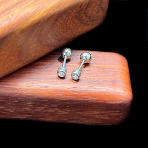 Macro shot of silver barbell cartilage earrings with round-cut cubic zirconia on wood