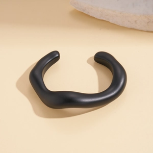 Macro detail of matte black irregular geometric wavy open cuff bracelet on stone base