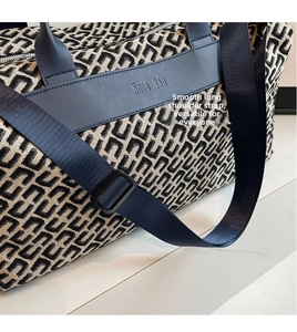 Dettaglio borsa da viaggio geometrica con cinturini in pelle blu scuro e logo inciso