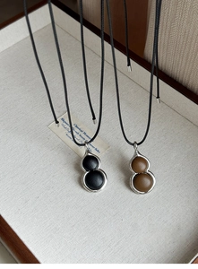 Macro detail of two gourd pendants in black and dark brown leather with metal frames