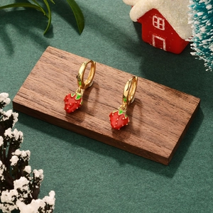 Close-up of golden hoop earrings with red strawberry pendants on a festive wooden surface
