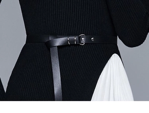 Détail d'une ceinture fine en cuir noir sur une robe en maille montrant la texture