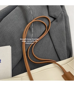 Detail of smooth brown long shoulder strap and fine stitching on a white tote bag