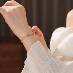 Detailed shot of gold bracelet with colorful zirconia flowers worn on woman's wrist