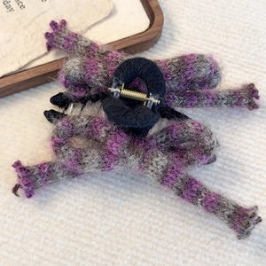 Detail of purple and grey striped knit bow hair claw with plush texture and golden spring