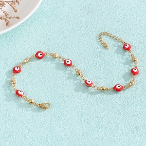 Detail of gold evil eye bracelet with red enamel beads on light blue background