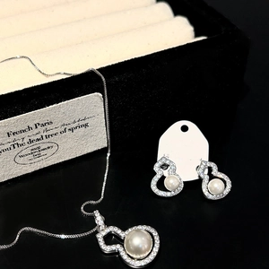 Macro shot of silver gourd necklace and earrings set with pearls and zircons on black surface