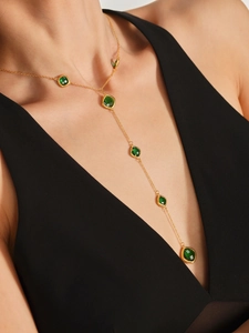 Dettaglio di una lunga collana a Y in oro con pietre preziose quadrate verde smeraldo