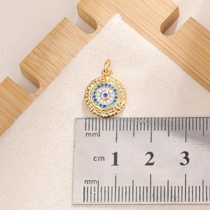 Macro detail of 10mm gold Evil Eye pendant with blue zircon stones on a white surface