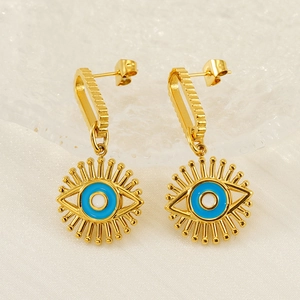 Close-up of gold-plated evil eye earrings with blue enamel detail on a white silk base