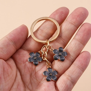 Close-up of golden keychain with three black flower charms held against peach background