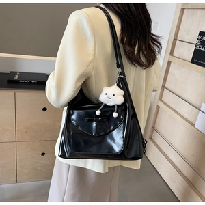 Close-up of black glossy leather tote bag with bow detail and cloud plush charm
