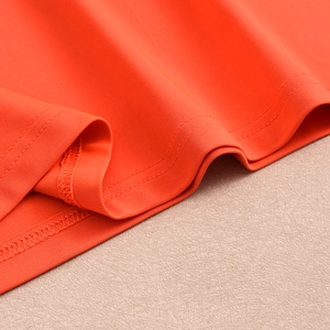 Detailed macro view of bright orange knit fabric with precise double-needle stitching hem