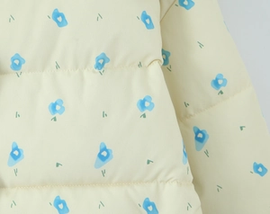 Detailed macro view of light yellow floral fabric with blue flower prints and stitching