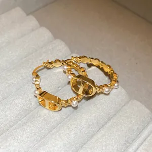 Elegant gold-plated hoop earrings with CD logo and white pearls on velvet display