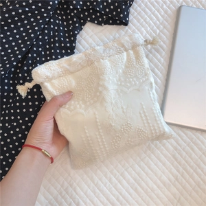 Close-up of white lace drawstring pouch with floral embroidery and tassel detail