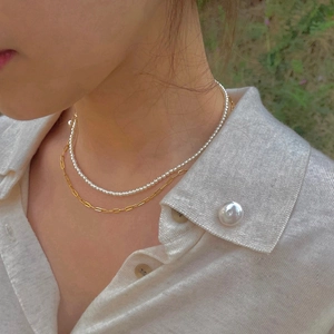 Close-up of double-layer necklace with gold chain and white mini pearls on a model