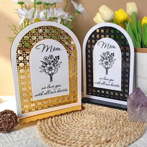 Detail of gold and black arched Mother's Day plaques on a woven mat with floral decor