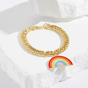 Detail of a gold chain bracelet with a colorful rainbow pendant on a white stone background