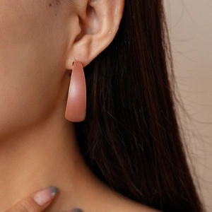 Close-up of matte dusty pink geometric hoop earring worn by a model with long dark hair