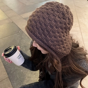 Detail of coffee brown chunky knit beanie with textured square weave and tassel earflaps