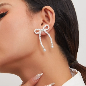 Close-up of elegant beaded bow earrings with pearls worn by a model in a studio setting