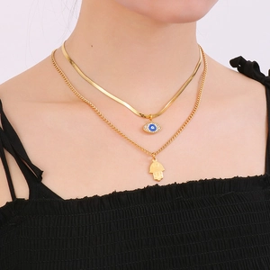 Detail view of double-layer gold necklace featuring Hamsa hand and blue evil eye charms