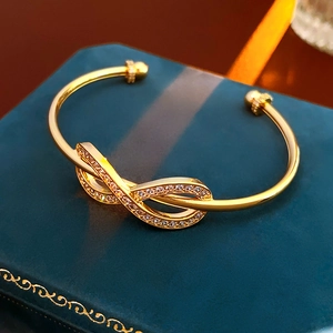 Macro detail of gold-plated infinity bracelet with cubic zirconia on green velvet