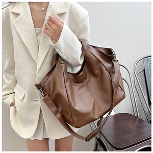 Detailed shot of large brown leather tote bag with adjustable strap worn with a beige suit